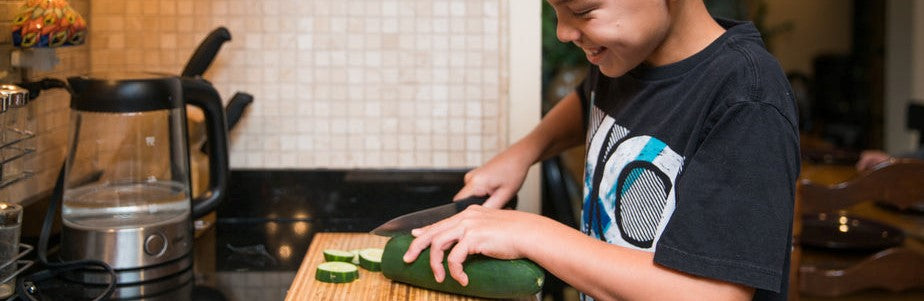 kid-helping-in-kitchen-cutting-cucumber-on-a-bread-board-with-small-kitchen-appliances-in-the-background